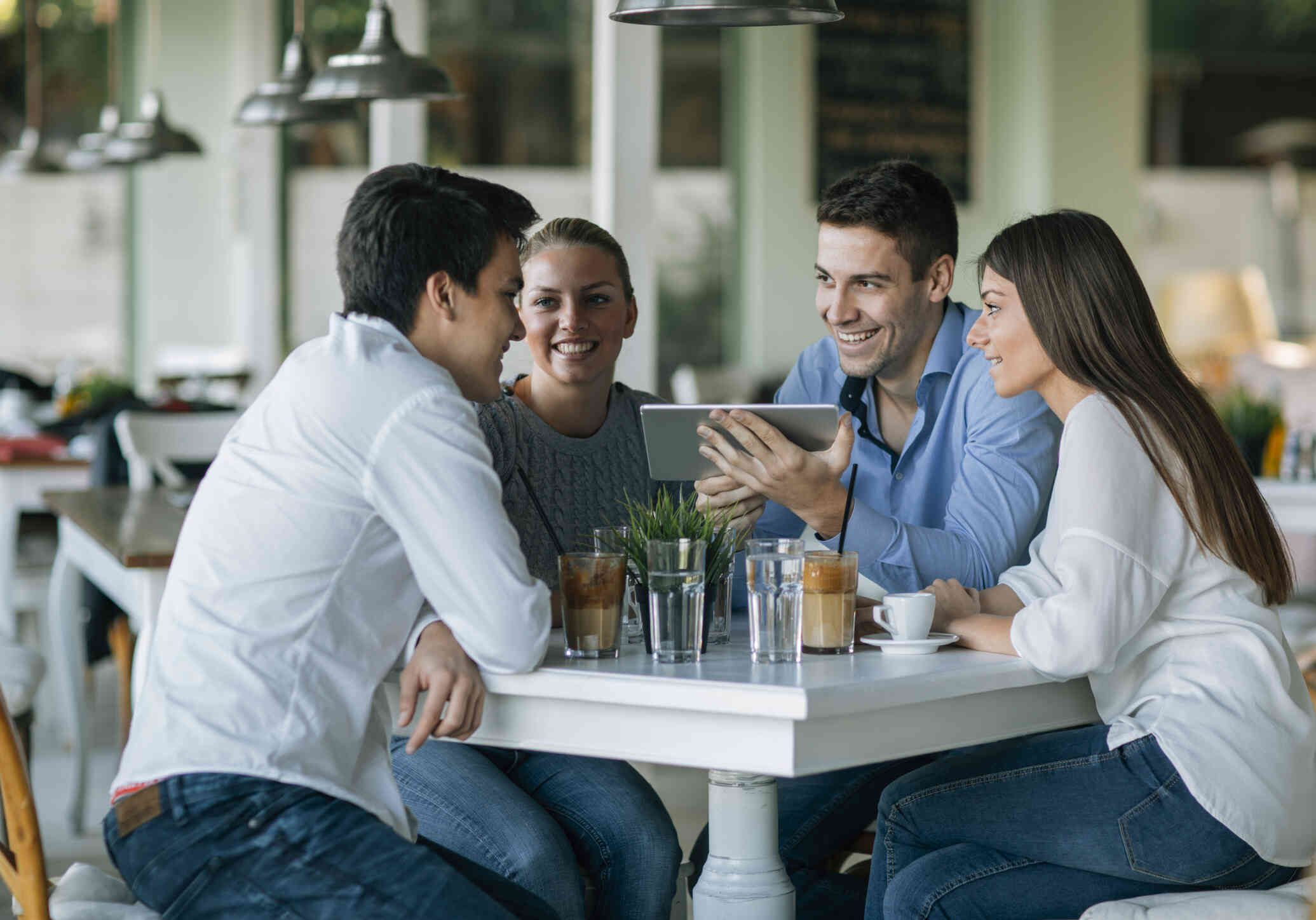 A group of young adults with positive expression sit around a table at a coffee shop engaged in a conversation